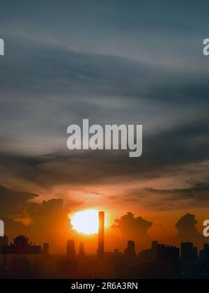 Vertical image, Sunset in the evening with dramatic shape and color of clouds and sky with Silhouette of cityscape, building skyline, nature backgroun Stock Photo