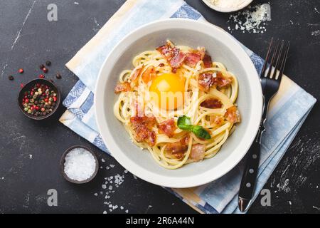 Traditional Italian pasta dish, spaghetti carbonara with yolk, parmesan cheese, bacon in plate on black rustic stone background, top view. Italian Stock Photo
