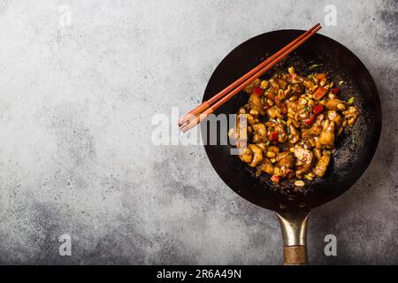 Top view of Kung Pao chicken, stir-fried Chinese traditional dish with chicken, peanuts, vegetables, chili peppers in a wok pan, space for text. Stock Photo