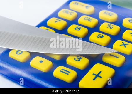 Knife blade placed on euro coin, calculator. Concept cutting rates, money business, crime. Macro. Stock Photo