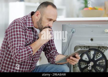 man using tablet to fix a washing machine Stock Photo