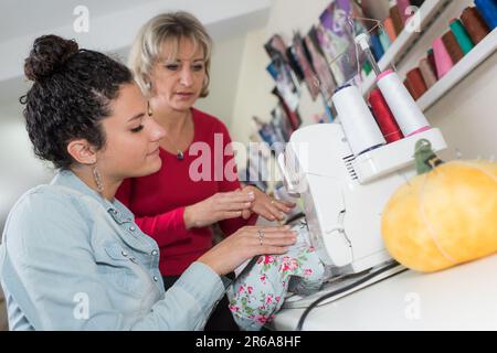 woman guiding younger lady using sewing machine Stock Photo
