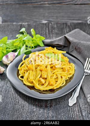 Spaghetti with pumpkin cream sauce, bacon, onion and garlic in a plate, towel, basil and fork on a black wooden board background Stock Photo