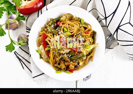 Spaghetti buckwheat soba with cabbage, champignons, sweet peppers, onions, garlic and green beans Asian-style in a plate on a napkin against backgroun Stock Photo