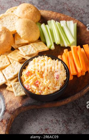 Pimento cheese is a versatile, creamy dip served with vegetables and crackers closeup on the wooden board on the table. Vertical Stock Photo