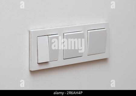 Block of three white plastic electrical switches on a white wall Stock Photo