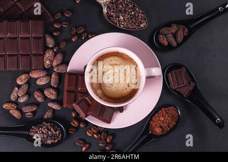 Aromatic cappuccino coffee cup with cafe beans, chocolate bar, cacao nibs on black background Stock Photo
