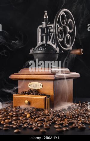 Vintage coffee grinder blender with cafe beans and aroma smoke isolated on black background Stock Photo
