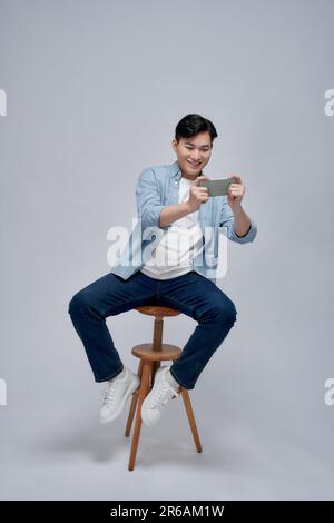 Full body profile side photo of young man sit on a stool play game cellphone over white background Stock Photo
