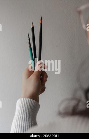 Woman's hands holding brushes. Concept of a person thinking about his next piece of art. Concept of painting and creative process. Stock Photo