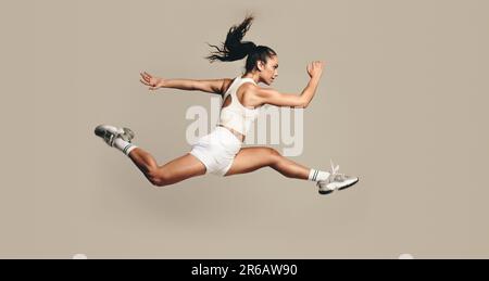 Active female athlete running mid air, vigorously working out in a studio. Sports woman combining strength and cardio exercises for better fitness and Stock Photo