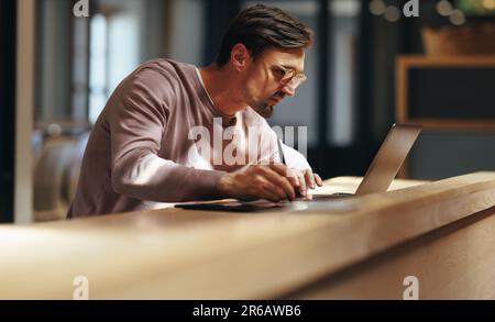 Focused graphic designer drawing on a graphics tablet in a cafe. business man working on a design with a laptop. Male design professional working remo Stock Photo