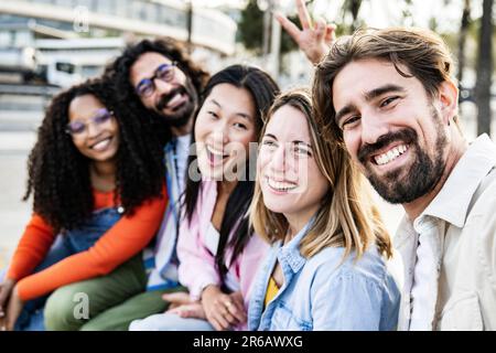 Diverse group of friends taking a selfie in the street sitting and looking at camera. Cheerful multiracial group of young hipsters taking a picture Stock Photo