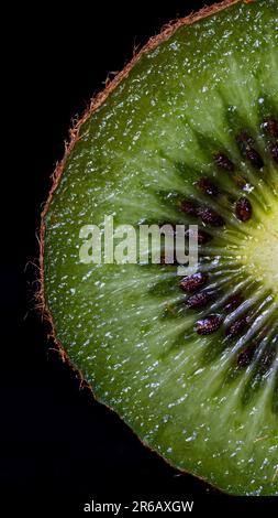 A freshly cut kiwi fruit is featured on a black background, showcasing its bright green flesh and black seeds Stock Photo