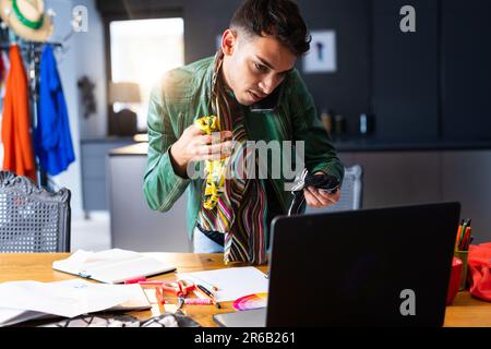 Biracial transgender fashion designer using laptop, talking on smartphone and holding fabric Stock Photo