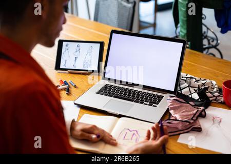 Close up of biracial transgender fashion designer using tablet and laptop with copy space on screen Stock Photo