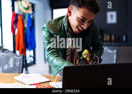 Biracial transgender fashion designer using laptop, talking on smartphone and holding fabric Stock Photo