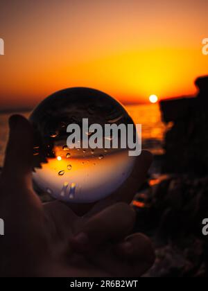 Glass round ball on the beach reflects the sea in summer at sunset ...