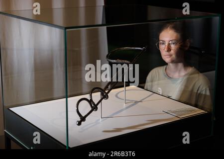Bramsche, Germany. 08th June, 2023. Exhibition assistant Lea Engel looks at a Roman neck fiddle (9 AD). In 2018, the Varus Battle Museum in Kalkriese found a Roman splint armor during excavations - according to the museum, the oldest so far and the only one preserved worldwide. The museum is showing other exhibits on this in the special exhibition 'Cold Case - Death of a Legionnaire' from June 10 to Nov. 5, 2023. Credit: Friso Gentsch/dpa/Alamy Live News Stock Photo
