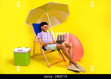 Full body cadre of young it specialist man using netbook lying sunbed satisfied his freelance job isolated on yellow color background Stock Photo
