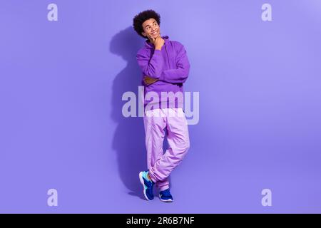 Full size photo of ponder pensive person wear violet hoodie sport pants look at empty space offer isolated on purple color background Stock Photo
