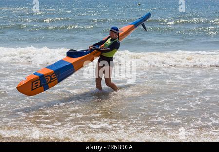 Young woman carrying a surf ski surfski, the Surf Life Saving GB GBR Beach Trial Weekend in the sea at Branksome Chine, Poole, Dorset, England UK in Stock Photo