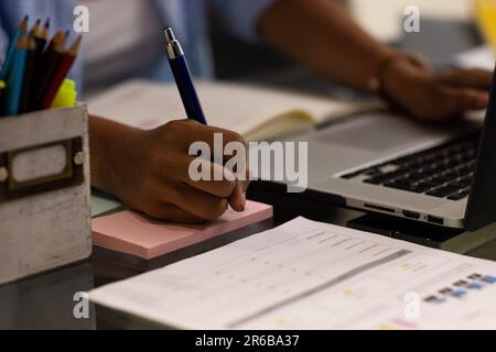 Midsection of busy biracial woman working at home sitting at table using laptop and making notes Stock Photo