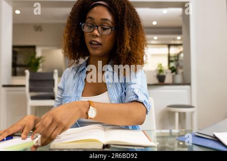 Biracial woman in glasses working at home, talking and looking at documents during video call Stock Photo