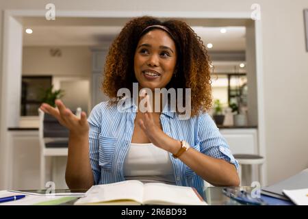Happy biracial woman working at home talking and gesturing during video call Stock Photo