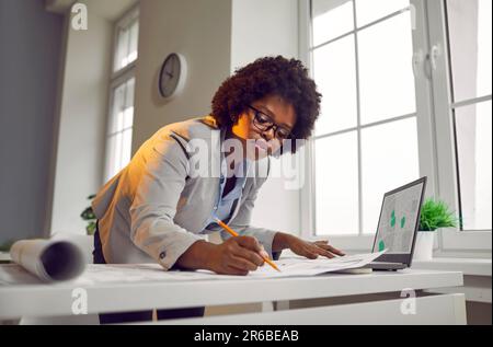 African American woman architect drawing blueprints in modern office Stock Photo