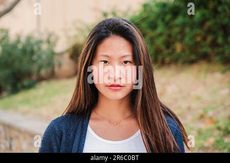 Individual close up portrait of serious young woman standing outdoors. One pensive teen female student looking at camera. Front view of a young chinese lady. Head shot of a proud teenage school girl. High quality photo Stock Photo