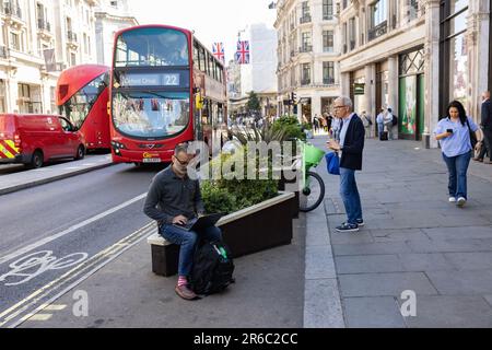 A man works on his laptop computer whilst sitting on a raised flower bed along Regent Street, central London, England, United Kingdom Stock Photo