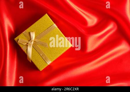Yellow gift box with a yellow ribbon and bow on a red fabric, silk background Stock Photo