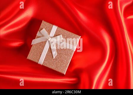 Brown gift box with a brown ribbon and bow on a red fabric, silk background Stock Photo
