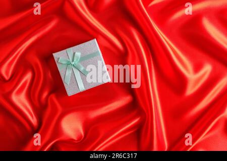 Silver gift box with a green ribbon and bow on a red fabric, silk background Stock Photo