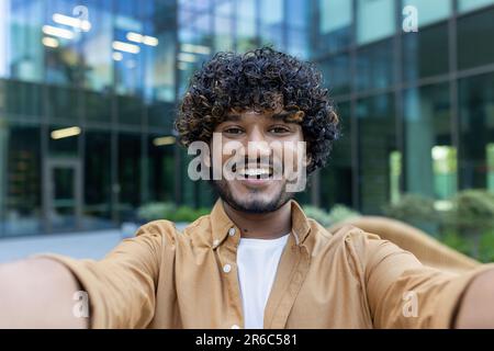 Online streaming. Close-up photo of a young Latin American man filming a blog, recording a podcast on the street. Smiling and talking to the camera. Stock Photo