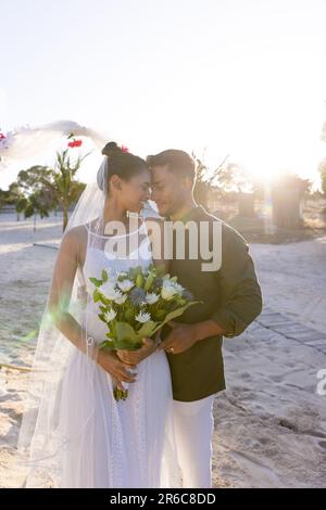 Smiling caucasian newlywed couple with face to face standing at beach at wedding ceremony Stock Photo