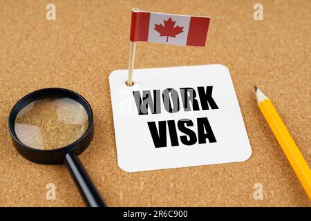On the table is the flag of Canada, a pencil, a magnifying glass and a sheet of paper with the inscription - Work Visa Stock Photo