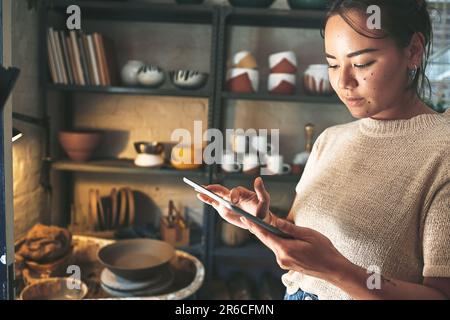 Technology allows me to work from anywhere in my studio. an attractive young business owner standing alone in her pottery studio and using a tablet. Stock Photo