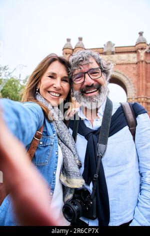 Vertical portrait happy senior tourist couple taking selfie outdoors in historical city.  Stock Photo