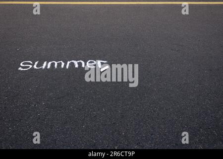 The word summer written on black asphalt with white chalk, with a yellow road marking line at the top of the photo. Stock Photo