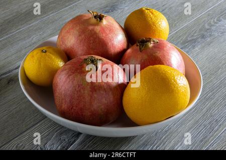Three of fresh ripe pomegranates and three oranges in a plate on a gray wooden table. Close-up Stock Photo