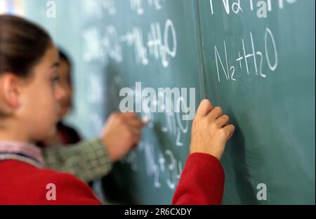 three pupils completing a science assignment on the schoolroom blackboard Stock Photo