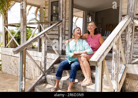 Ecstatic caucasian senior couple talking and laughing while sitting on staircase outside cottage Stock Photo