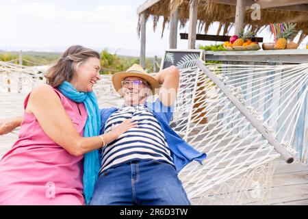 Caucasian senior couple laughing and lying on hammock at beach, copy space Stock Photo