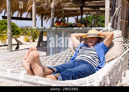 Caucasian senior man with hands behind head sleeping on hammock at beach Stock Photo