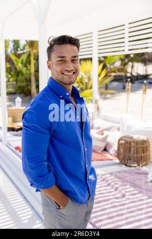 Handsome caucasian young man with hands in pockets smiling and standing at tourist resort Stock Photo