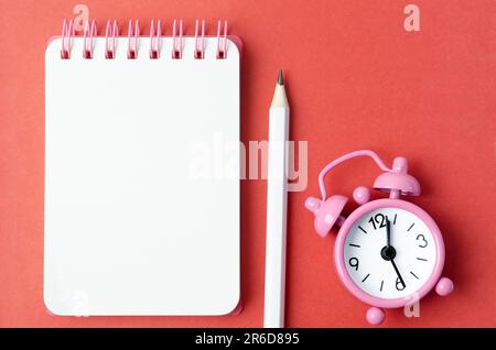 Blank open diary and Alarm clock with pencil on red colored background Stock Photo