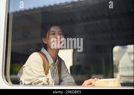 A pretty and happy young Asian female traveler or backpacker sits in her seat on a train, traveling alone to somewhere. Summer vacation concept Stock Photo