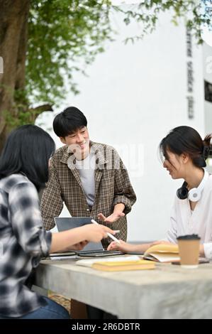 A handsome and cheerful young Asian male college student is discussing work with his friends and sharing his ideas while working on their group projec Stock Photo